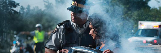 Un policier ?loignant une citoyenne de la fum?e. On voit une ambulance et un policier en arri?re-plan