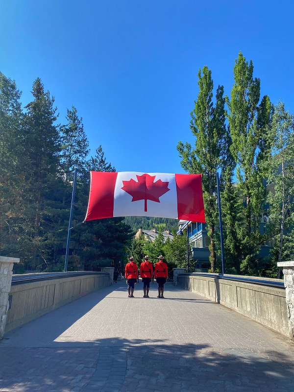 A photo of three RCMP members in red serge under a Canadian flag
