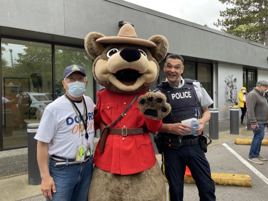 Richmond RCMP officer and volunteer posing with Safety Bear outside the community police office