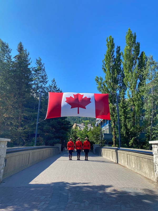 Une photo de trois membres de la GRC en tunique rouge debout sous un drapeau du Canada.